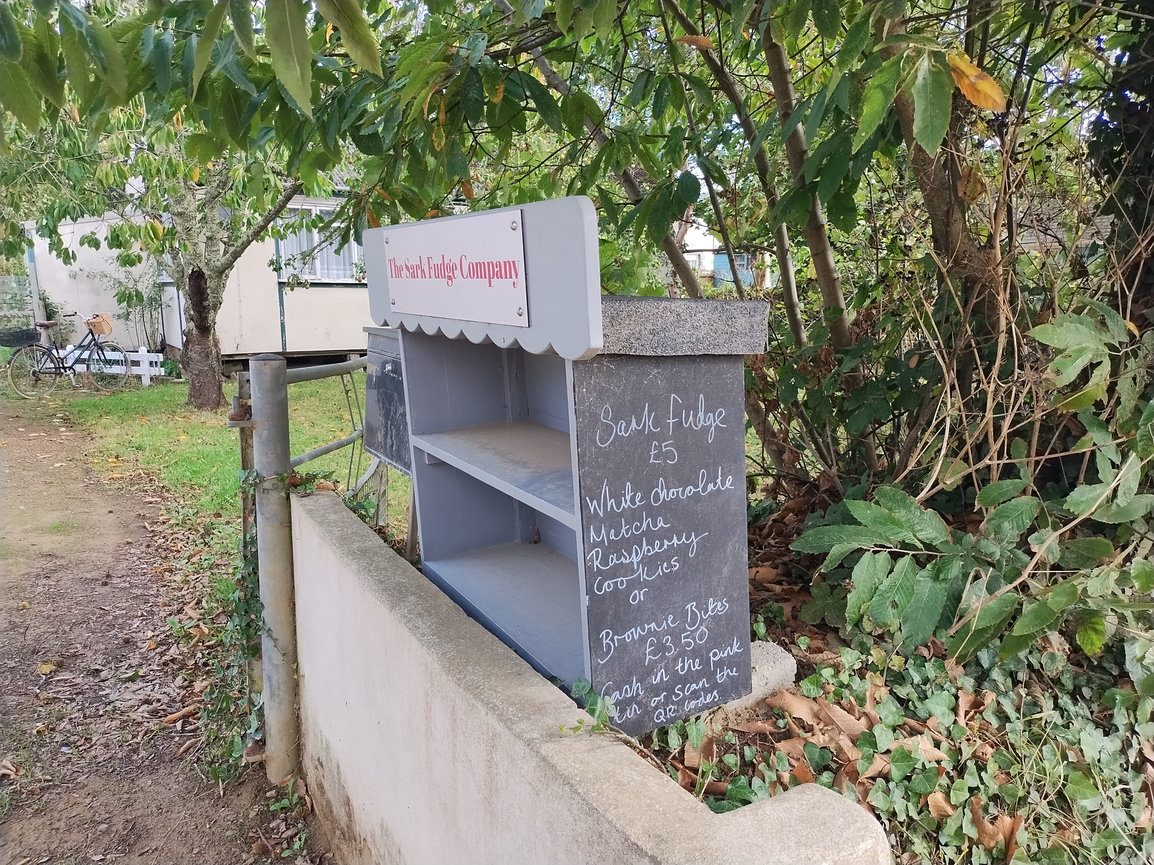 A chalkboard offers sales of baked goods from a box, payment goes in a tin or via QR codes